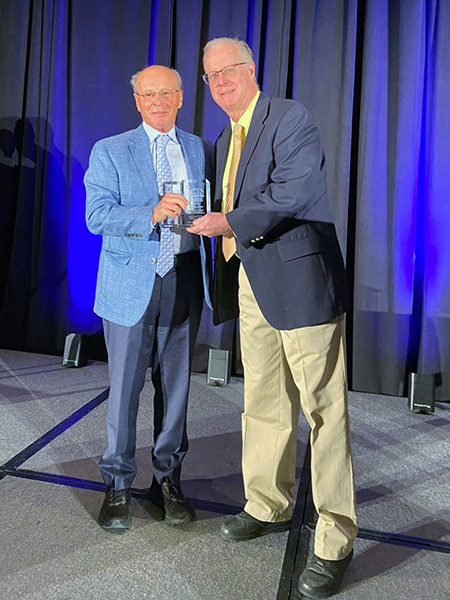 Two men on stage holding a clear glass award.