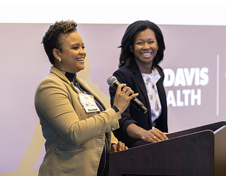 Two women at a podium with large screen behind them that reads &ldquo;UC Davis Health&rdquo;.