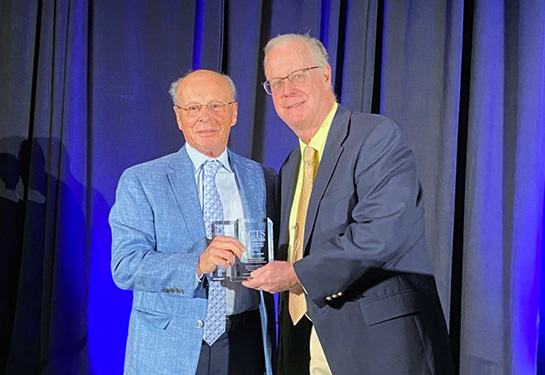 Two men on stage holding a clear glass award.