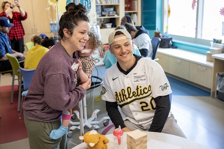 An A's player smiles next to a woman holding a baby.