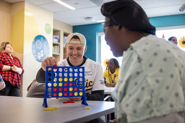 An A's player plays checkers with a pediatric patient.