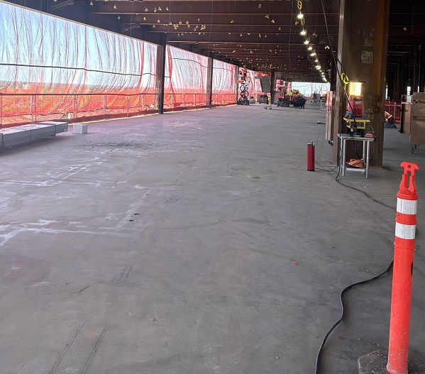 Interior floor space showing unfinished concrete floor, temporary lighting and safety barriers along the perimeter.