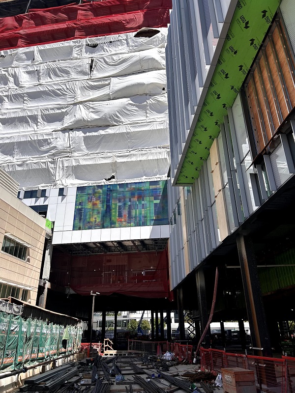 Ground-level view looking up at the tower with exterior wrap, fa&ccedil;ade installation and construction staging below.