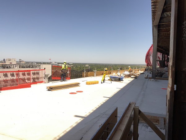 Rooftop construction area with workers, safety barriers and materials staged on a flat concrete surface.