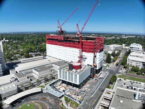 Aerial view of California Tower under construction with red safety netting, white exterior wrap and two cranes above the structure on the Sacramento campus.