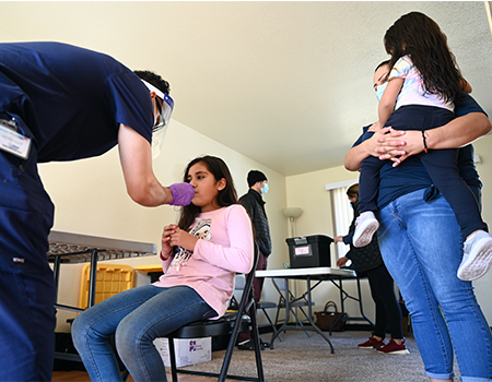 A girl next to her mother gets Covid nasal test by health worker at an indoor vaccination apartment in a migrant housing complex.