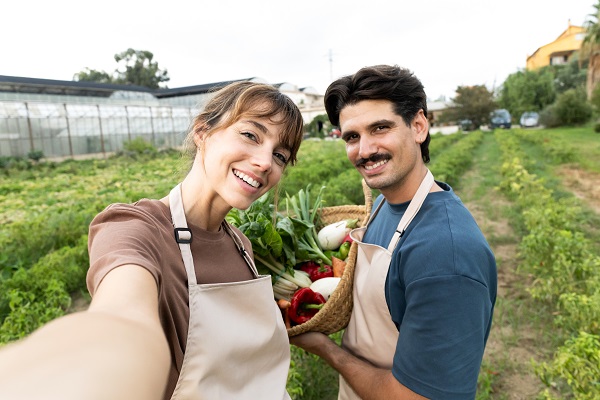 Two people hold a basket of freshly harvested produce while standing in a cultivated garden field.