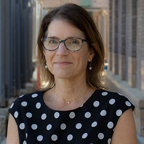 Aubyn Stahmer, in a black and white polka dot shirt, with brown hair, smiles for the camera.