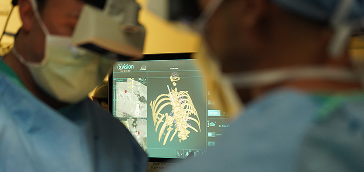 Two surgeons operate wearing headsets; the screen behind them shows the 3D augmented reality projection they see.