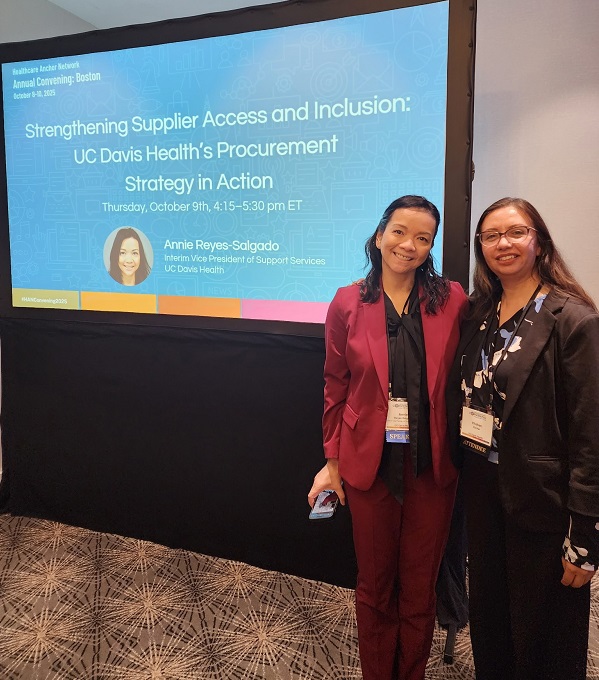 Two attendees stand in front of a presentation screen titled &ldquo;Strengthening Supplier Access and Inclusion: UC Davis Health&rsquo;s Procurement Strategy