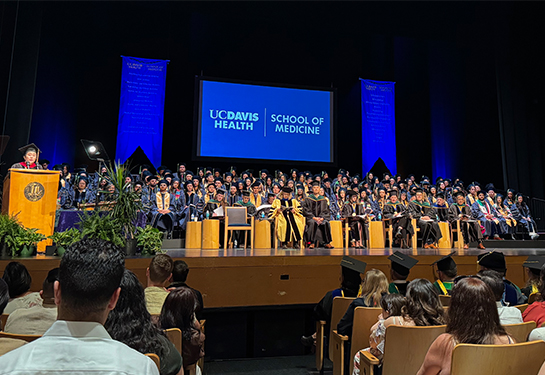 A total of 119 students seated on stage listening to a UC Davis faculty member speak from podium 