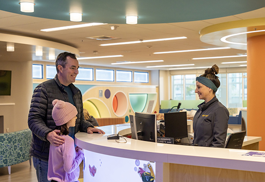 Parent and child stand at counter, while a person checks them in.