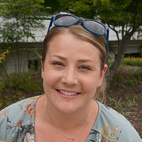 Headshot of a smiling woman with sunglasses on her head, a light green shirt and a gold chain.