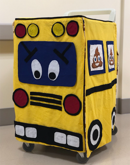 A felt cart cover designed to look like a school bus but with eyes on the windshield and poop emojis on the side.