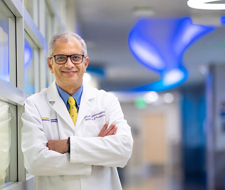 Man in white coat folds arms and smiles at camera