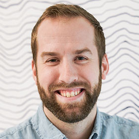Nick Card, in a blue shirt, with a beard, smiles for the camera. 