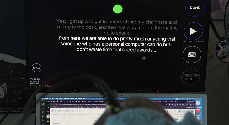 A computer screen, part of a brain-computer interface setup, is displayed while a  man sits in front of it.