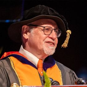 Dean Cavanagh in graduation regalia at podium