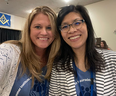 Two women stand together, posing for a selfie at a conference. 