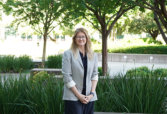 A person stands outside in front of trees and greenery
