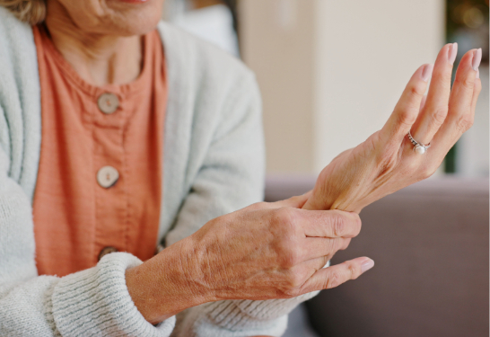 An older adult gently holding and rubbing one wrist with the opposite hand, suggesting joint discomfort or pain.