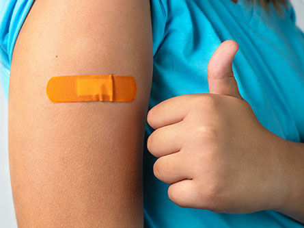 Child shows thumbs up near vaccination patch
