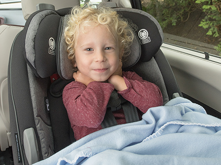 Child smiling in a car seat with blanket over the top