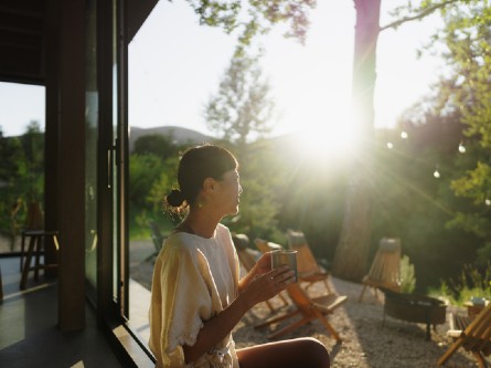 A woman holding a mug of tea while looking at a sunrise.