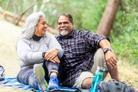 A senior couple enjoying a picnic on a blanket in the woods.