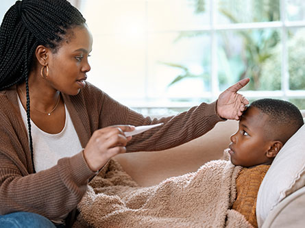 Mother taking her son's temperature with a thermometer as he's sick with a fever