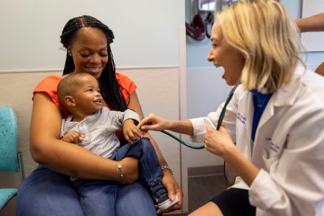 A pediatric patient and their mother smile at a pediatric primary care provider.