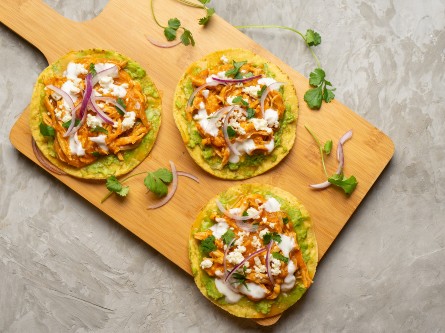 Three buffalo chicken tostadas on a wooden board