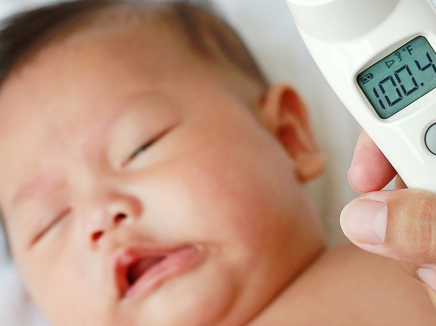 baby with person holding thermometer in front reading 100.4