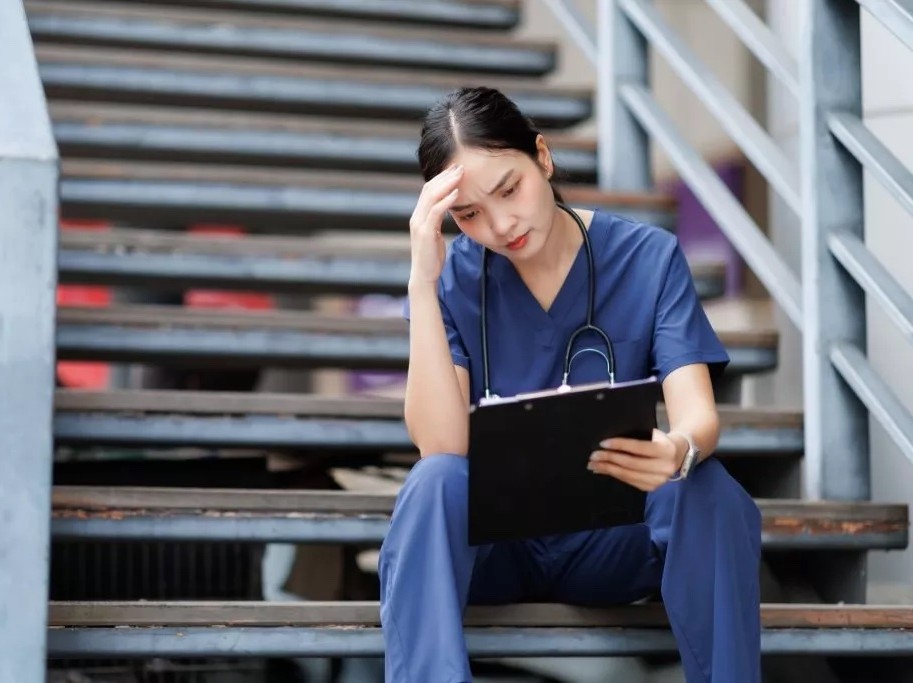 person sitting on stairs in scrubs holding clipboard
