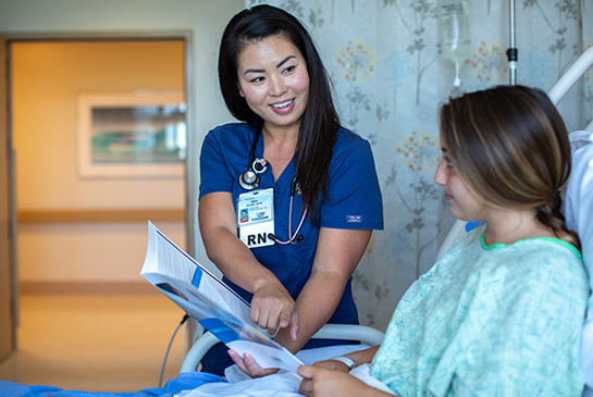 A nurse bedside, speaking with a patient. 