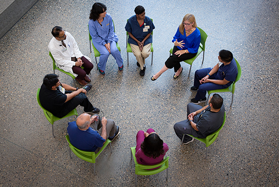 A group of peole sitting on a circle of chairs.