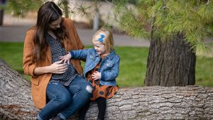 Pregnant mother sitting at a park bench with her daughter touching her stomach.