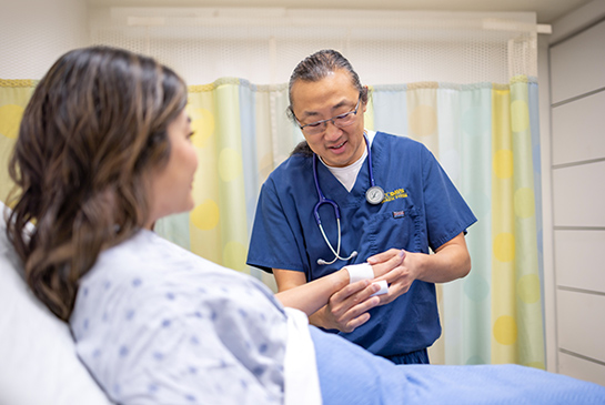 Patient in bed and a nurse bandaging her hand.