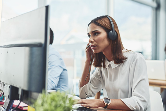 A woman working at a computer screen and talking on the phone.