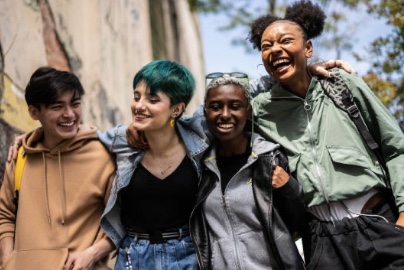 Group of four diverse, young adults walking together shoulder to shoulder 