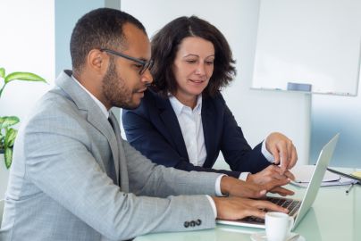 two professionals sitting side by side at a desk looking at a laptop computer screen