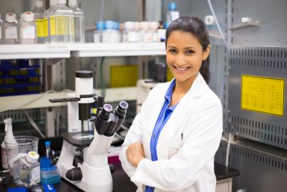 Person in a lab coat standing next to a microscope.