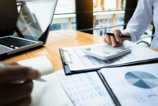 person using calculator on top of notebook and papers on desk 