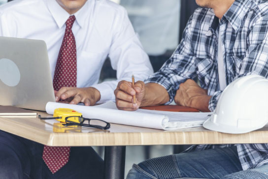 close up shot of people sitting around a table with a computer and blueprints
