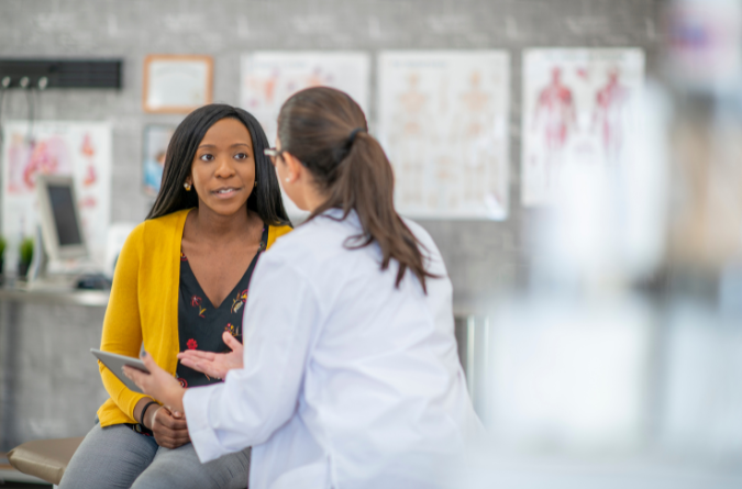 Two women, a doctor and patient, talk in a bright room. 