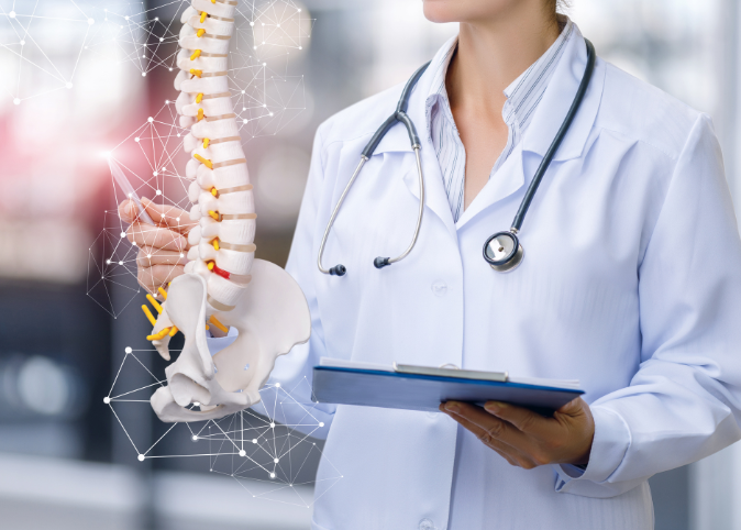 A doctor in a white coat with a clip board motions toward a graphic of a human spine.