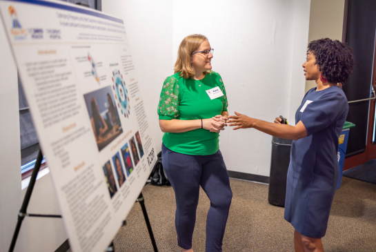 Two women talk next to a research poster at the Rev PC Summit.