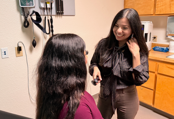 A doctor in jeans and a black button down shirt smiles at a patient whose face is not shown.