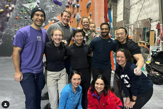 A group of residents and fellows with a rock climbing wall in the background.