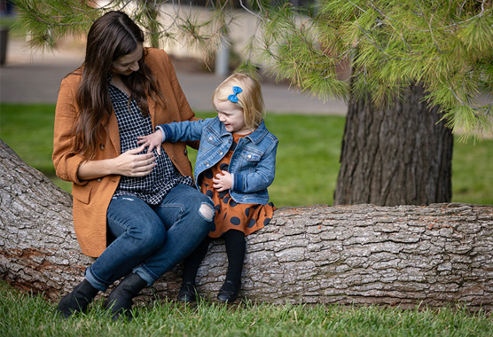 Pregnant mother and her small child sitting together on a log.
